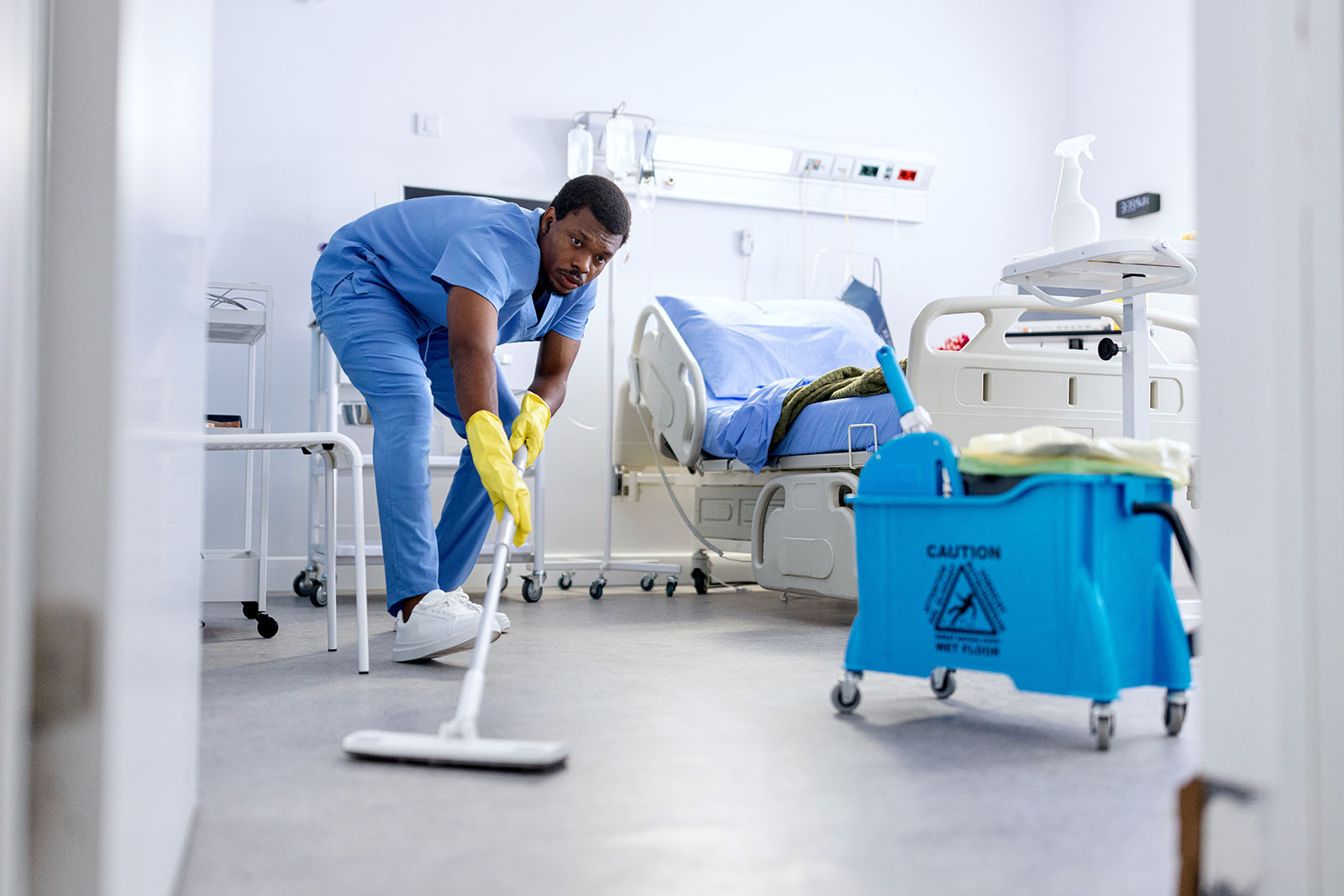 A dedicated staff member cleans the floor of a hospital room